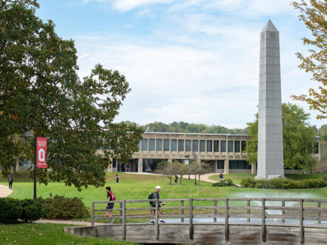 Scene on the Newark campus with students crossing over a bridge in front of a building and a tower